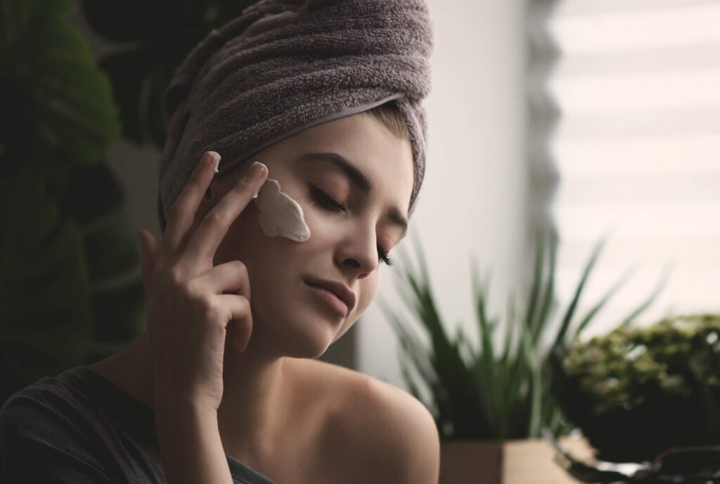 Young woman applying cream on face